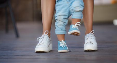 44560554 - the first steps of the kid, mom in white sneakers with a young son, dressed in blue pants and blue shoes, a warm summer day and learn to walk in the street, the first steps, the mother maintains her son.